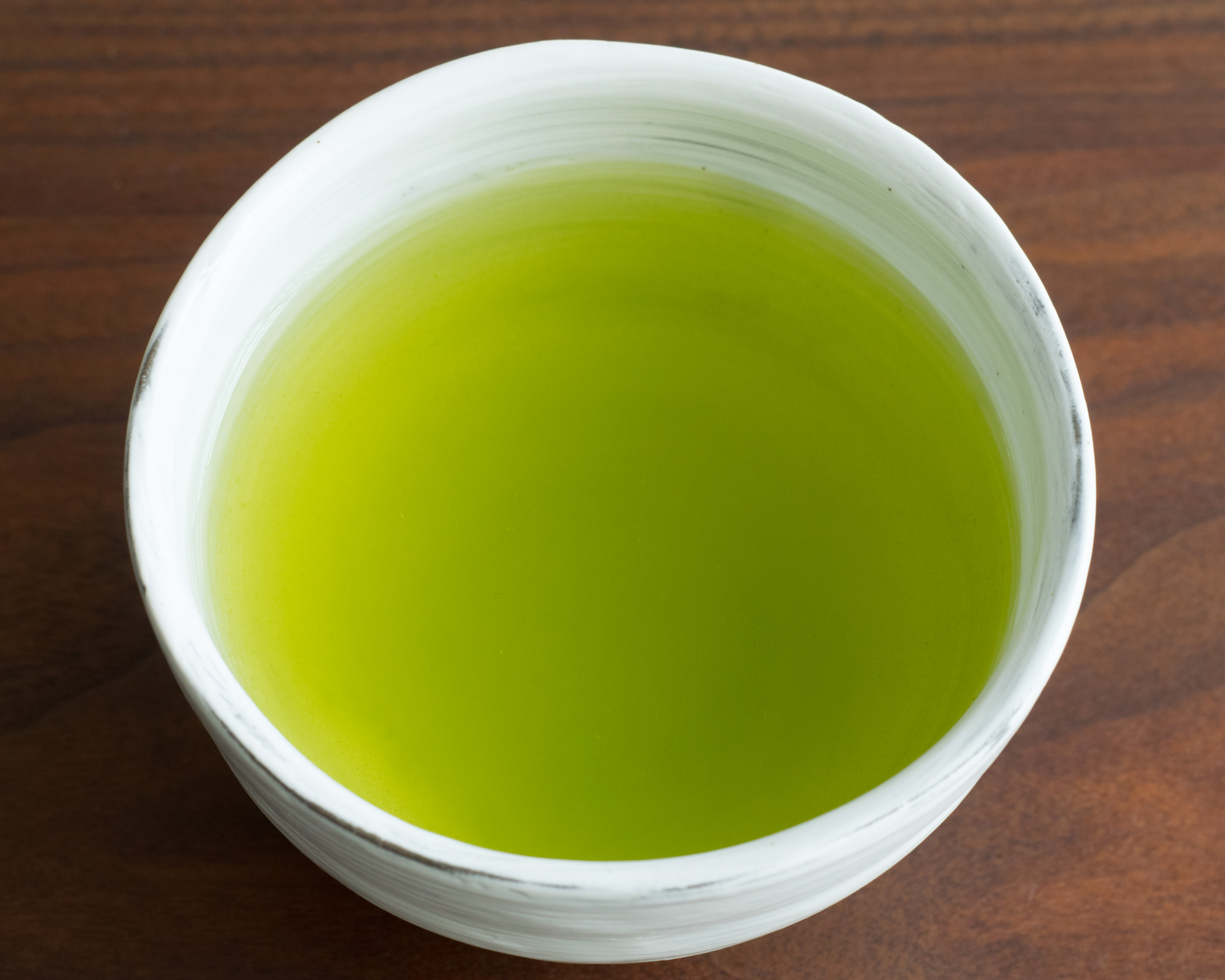 A white cup of bright green Japanese sencha tea seen from above