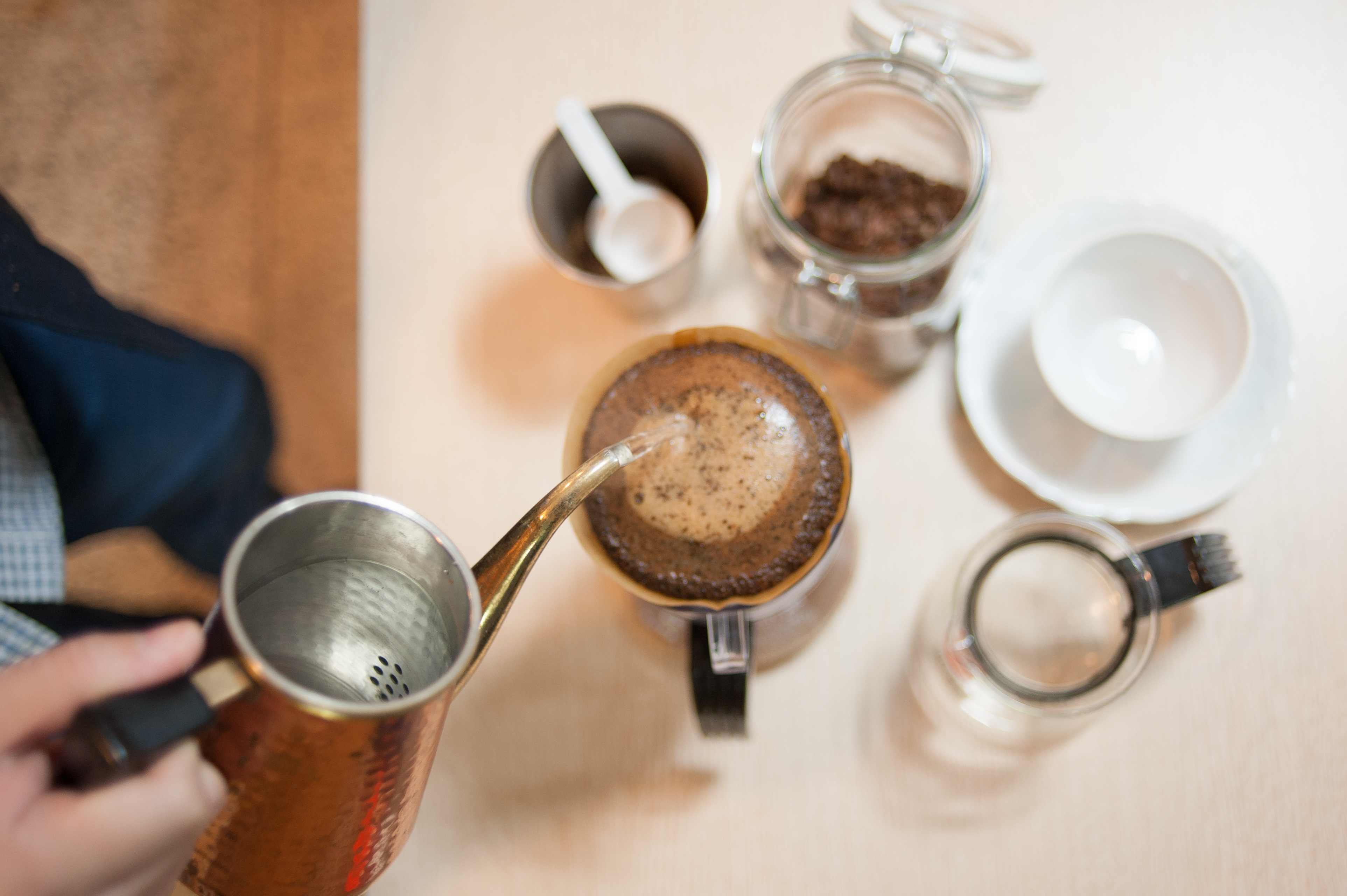 Overhead view of hot water poured from a copper kettle into a pour-over cone filled with coffee grounds