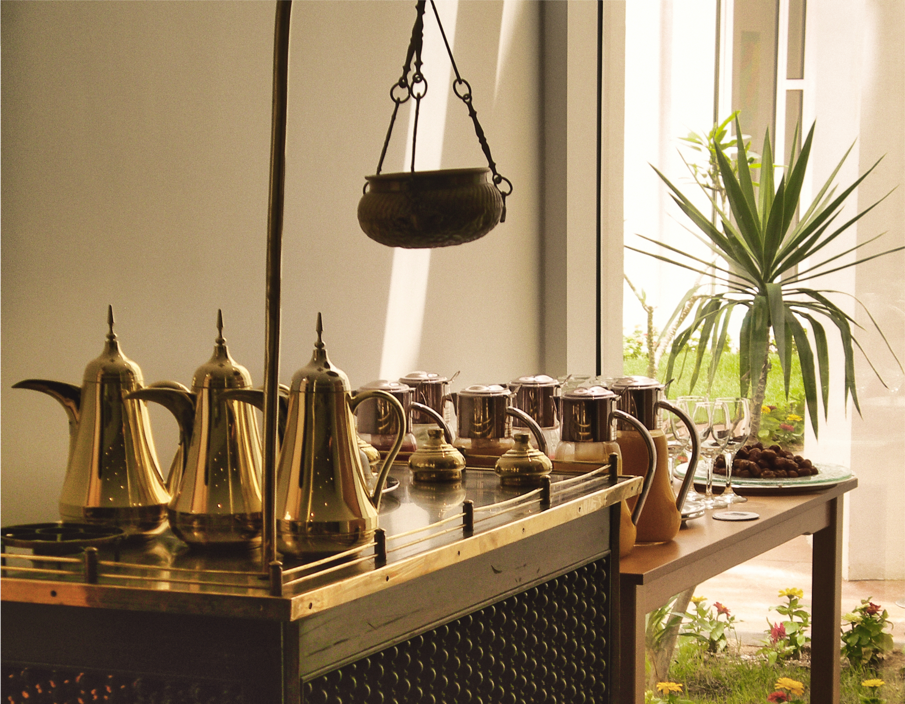 A row of brass dallah coffee pots on a serving counter beside a plate of dates and small glasses