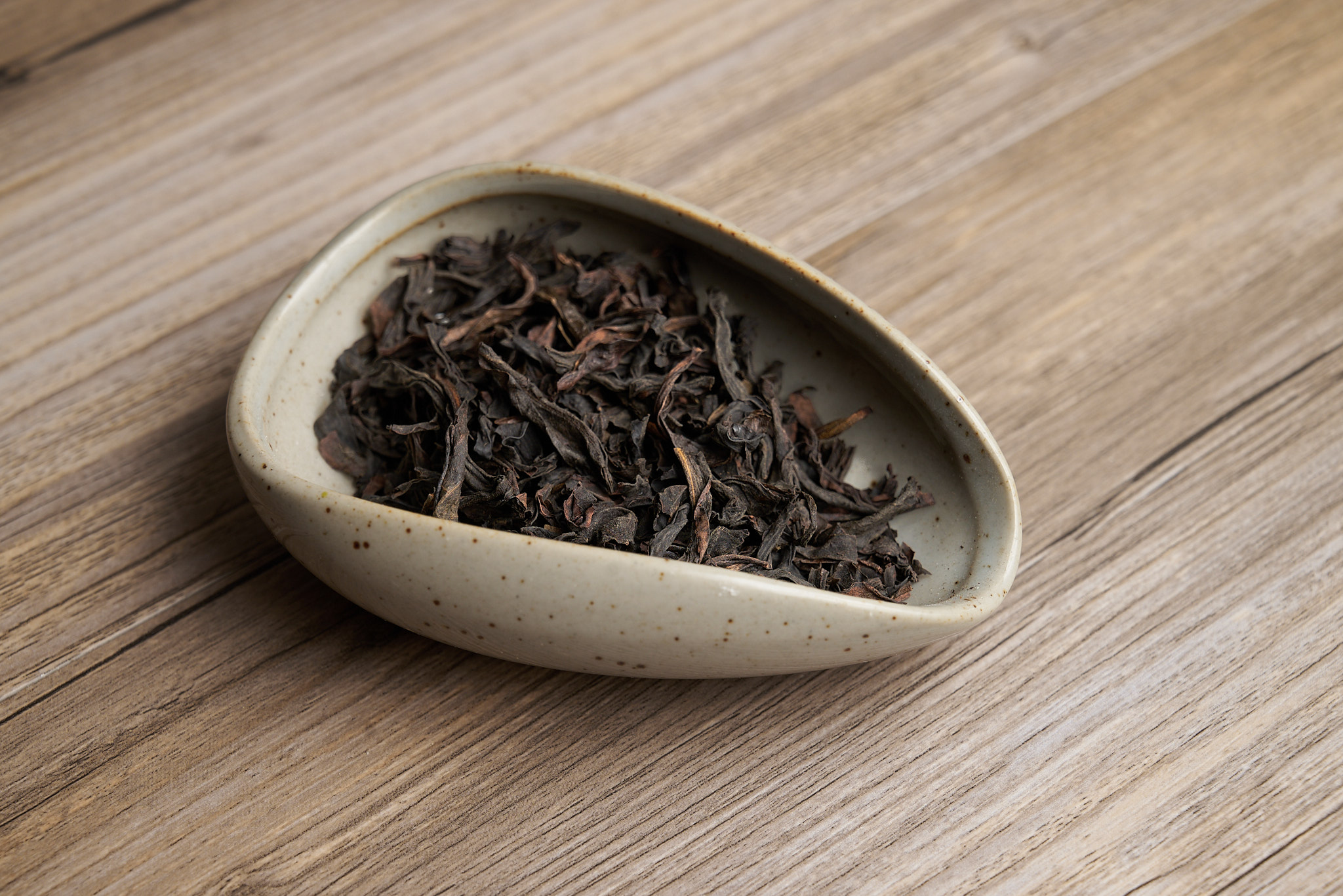 Dark twisted oolong tea leaves in a speckled ceramic tea scoop on a wooden table
