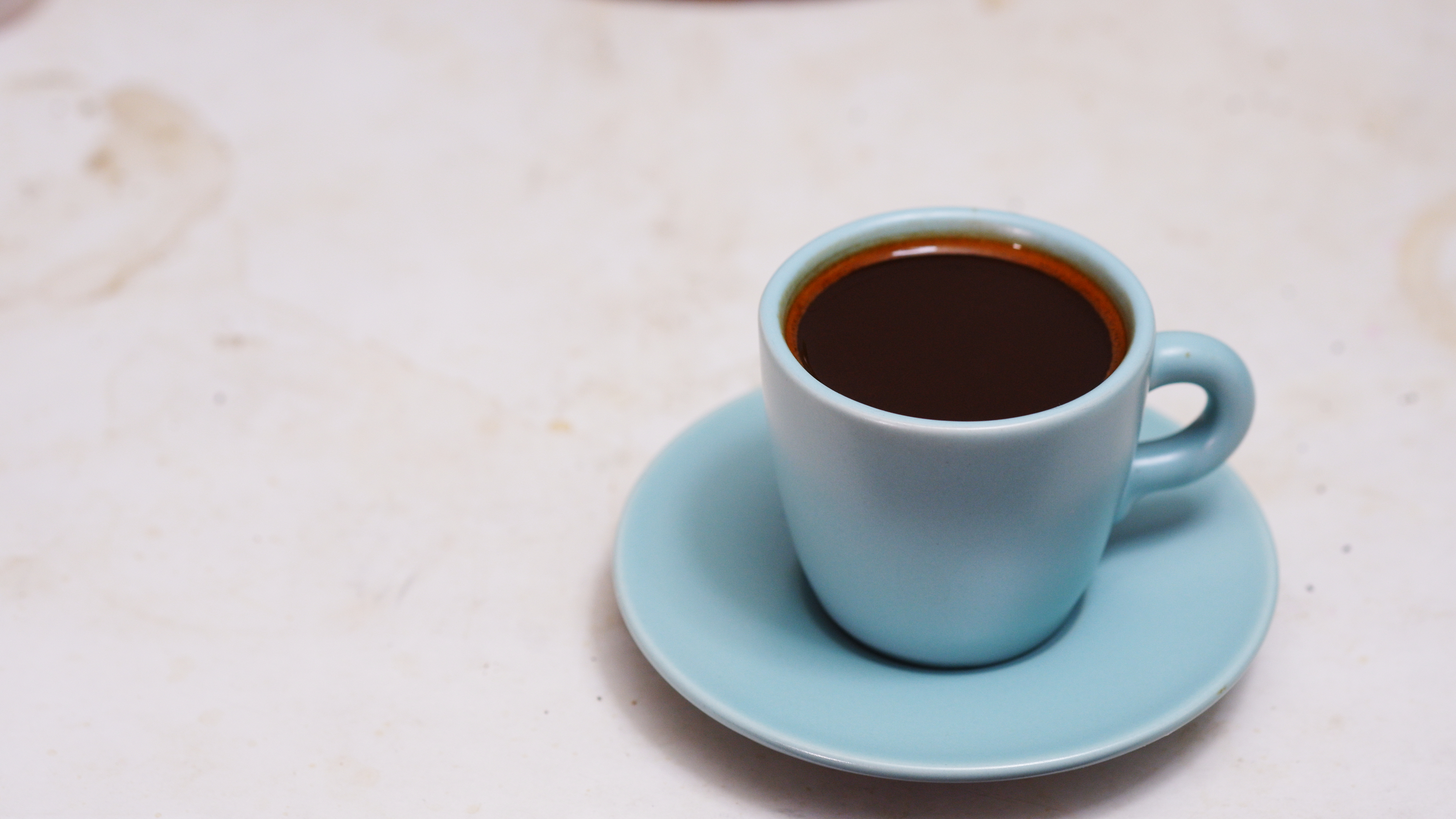 A small pale blue cup of black coffee on a matching saucer on a pale stone counter