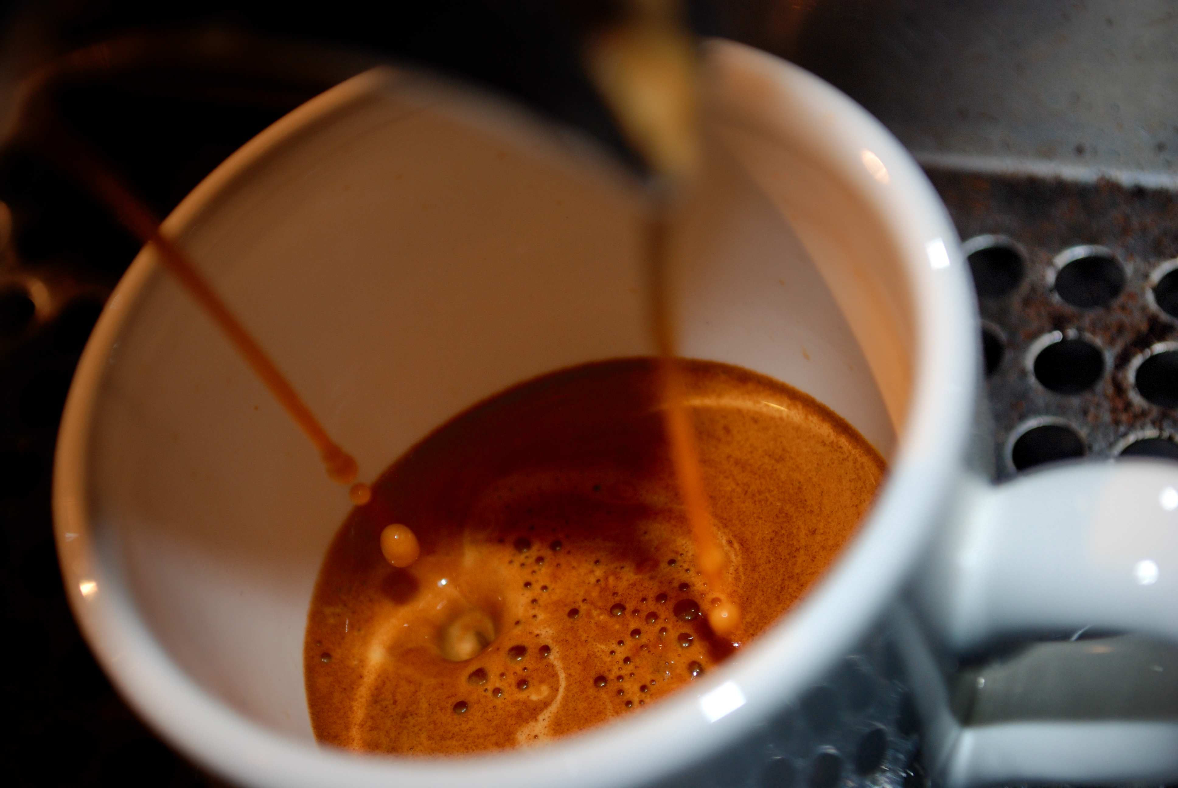 Two streams of espresso pouring into a white cup and forming a golden crema