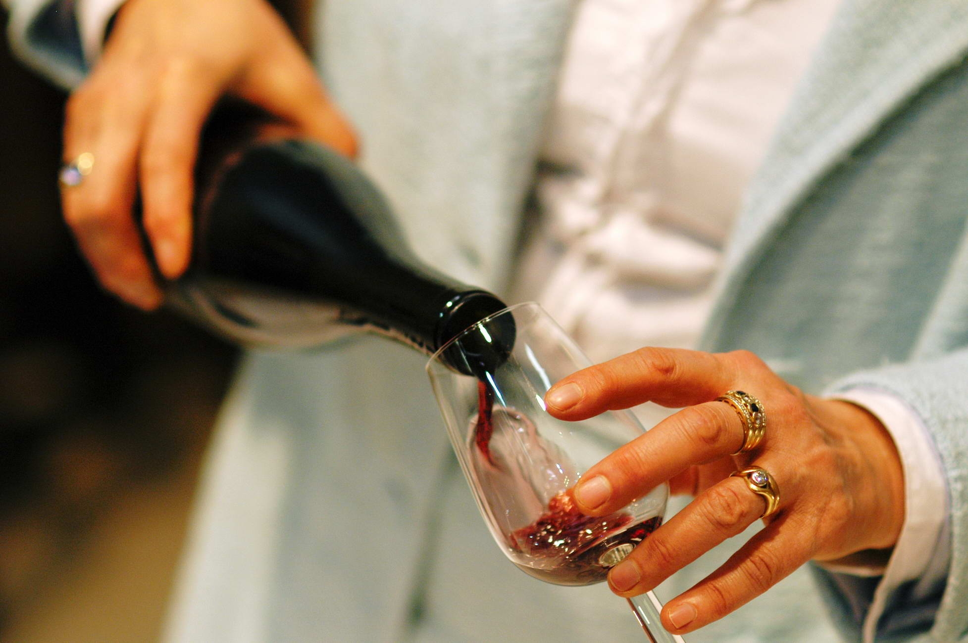 A hand pouring red wine from a dark bottle into a stemmed glass held by another hand