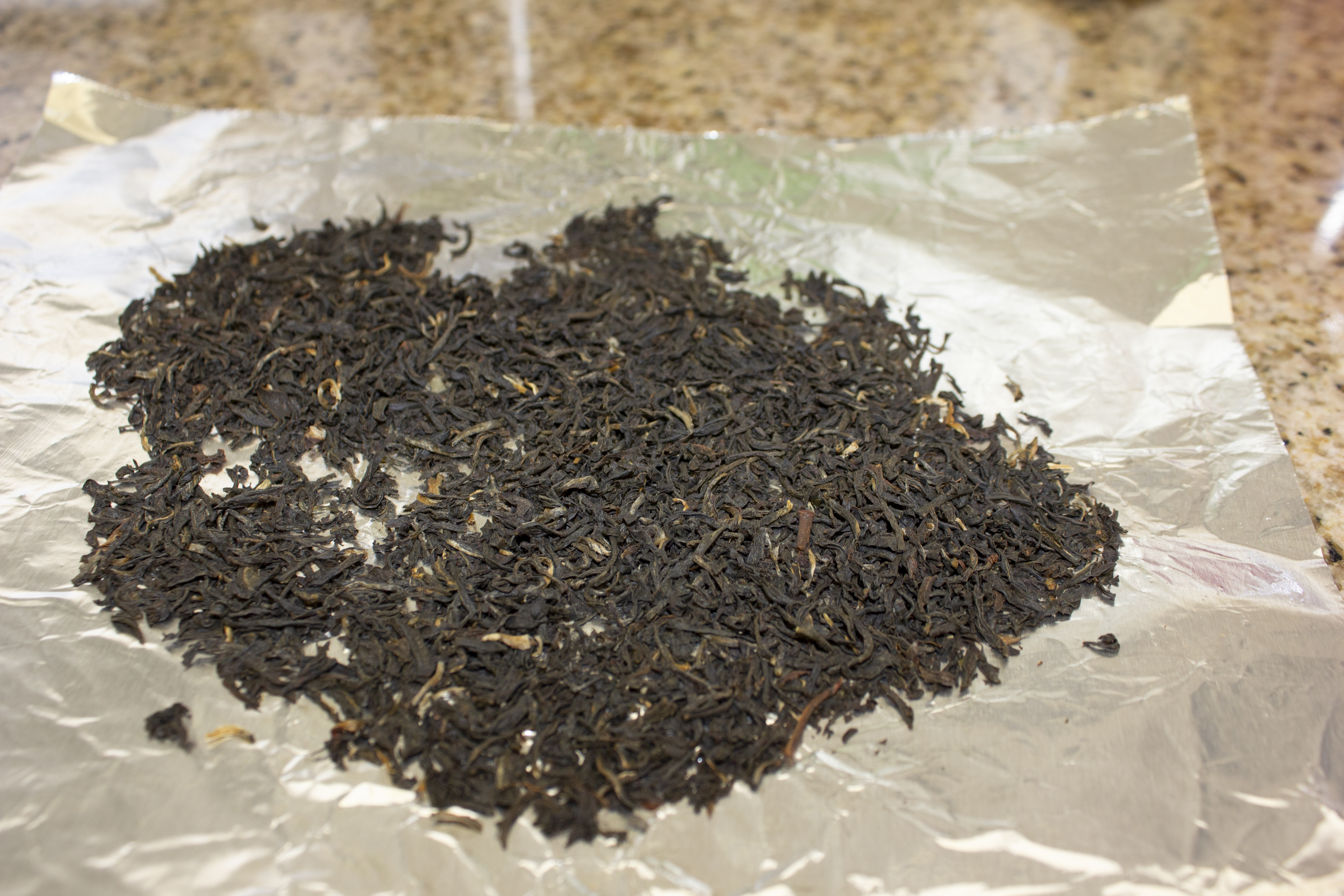 A small heap of dry black tea leaves spread on kitchen foil