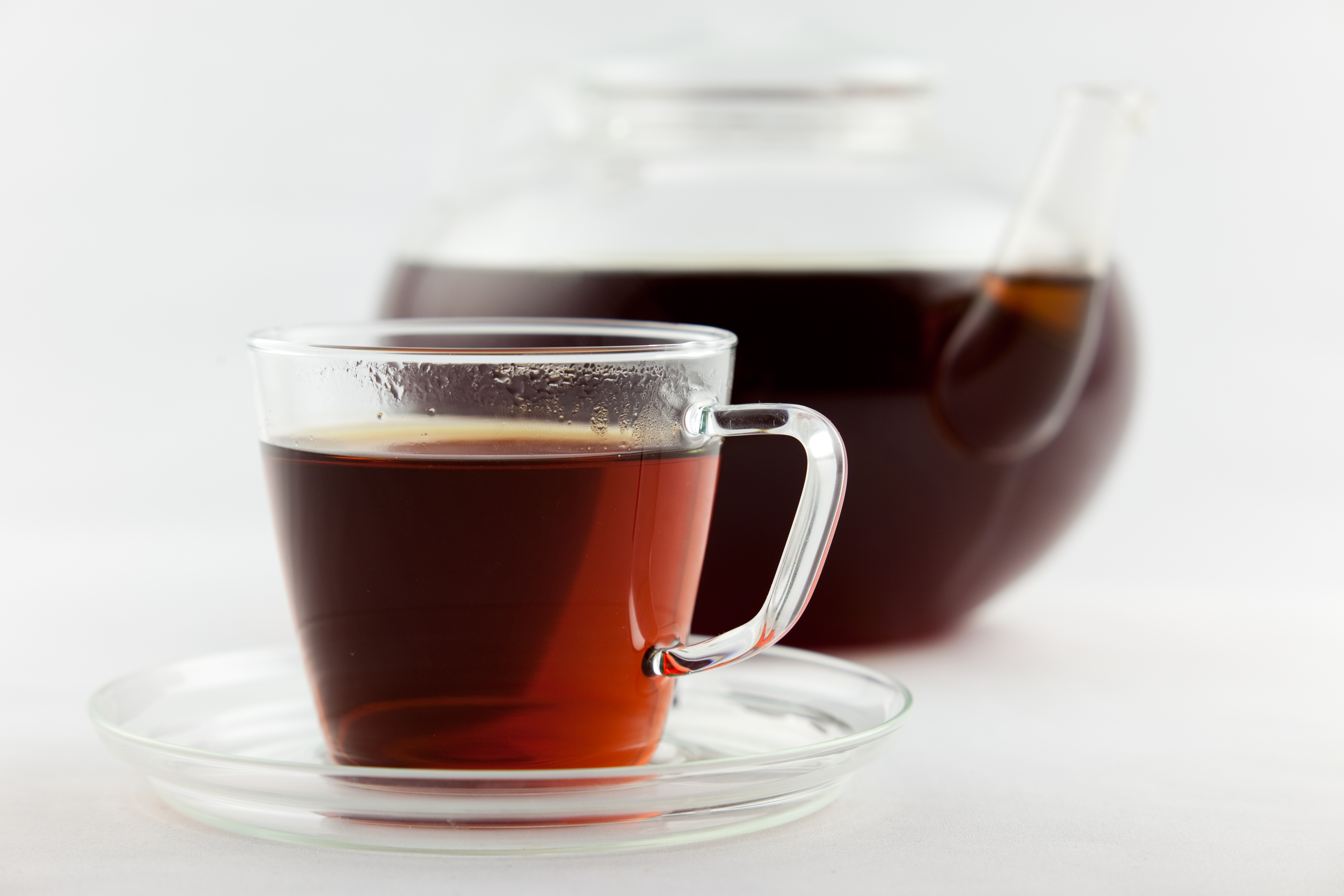 A clear glass cup of red-brown rooibos tea in front of a glass teapot
