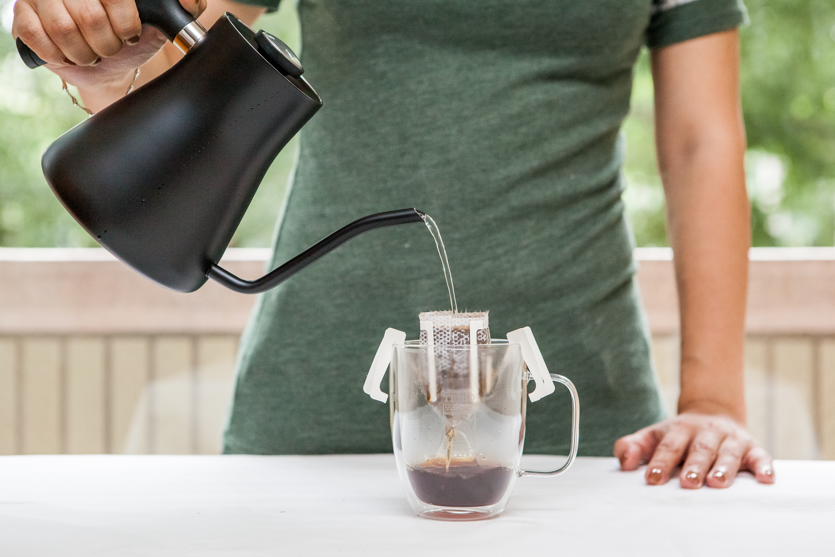 Hot water poured from a gooseneck kettle into a single-cup pour-over filter on a glass mug