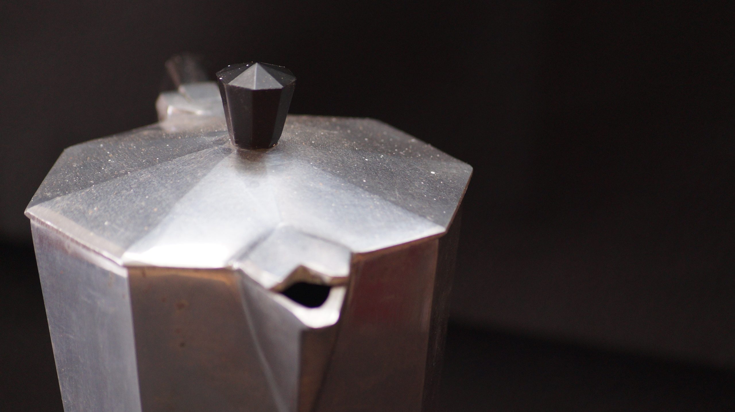 Close view of the faceted aluminum lid and spout of a stovetop moka pot