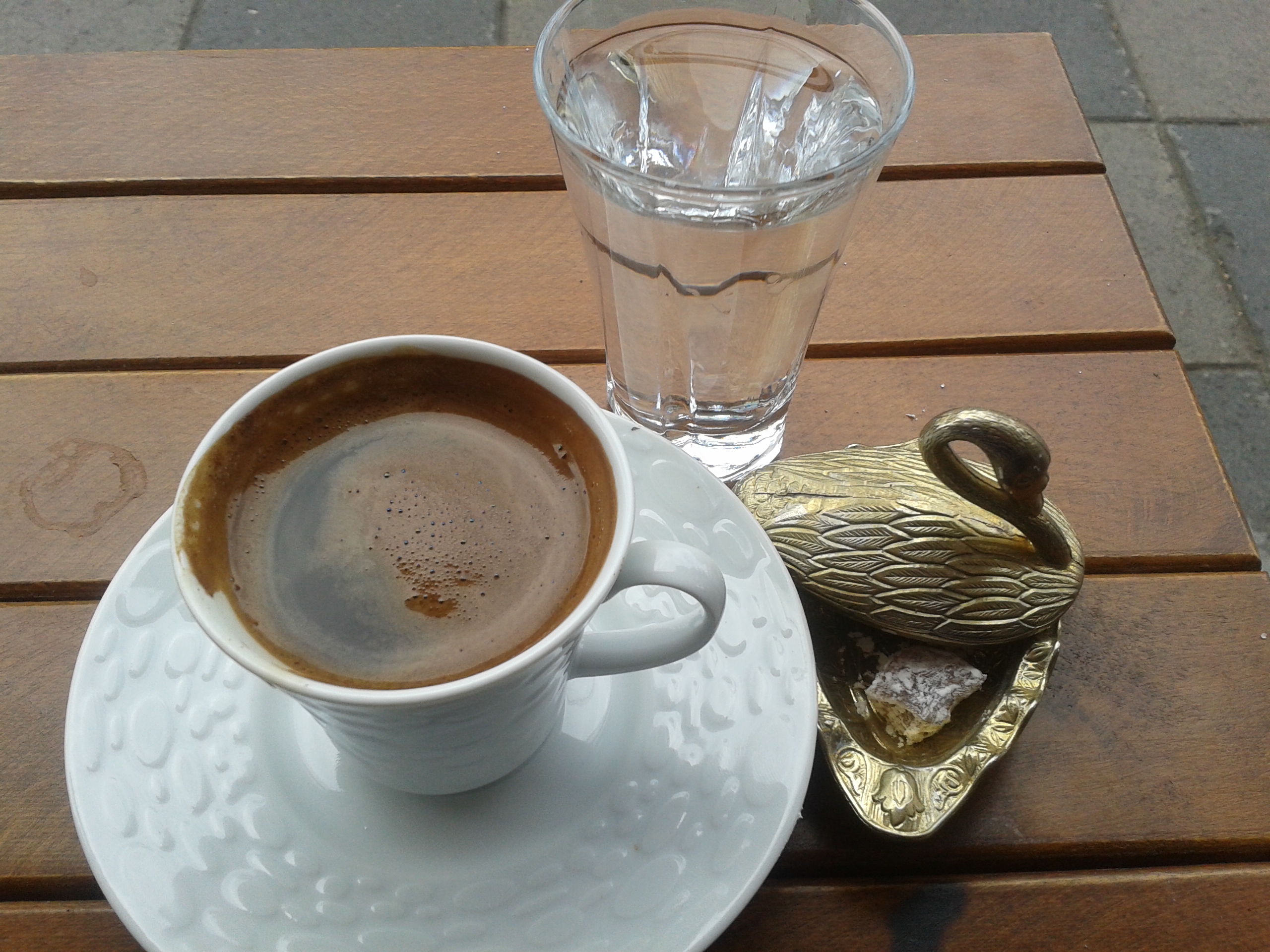 Turkish coffee in a white cup with a glass of water and a piece of Turkish delight in a small brass dish