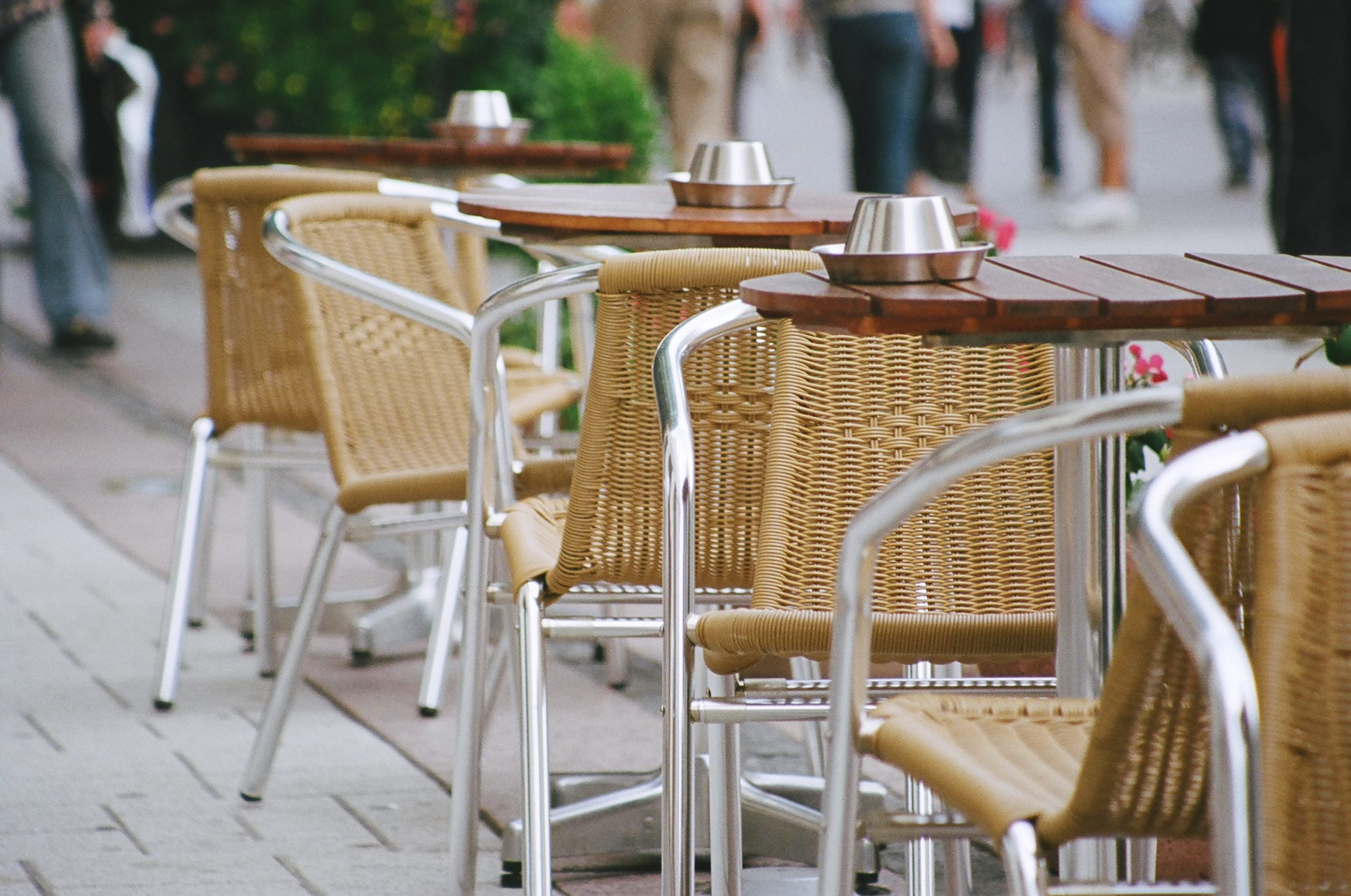Rows of wicker cafe chairs and wooden tables set out on a city pavement