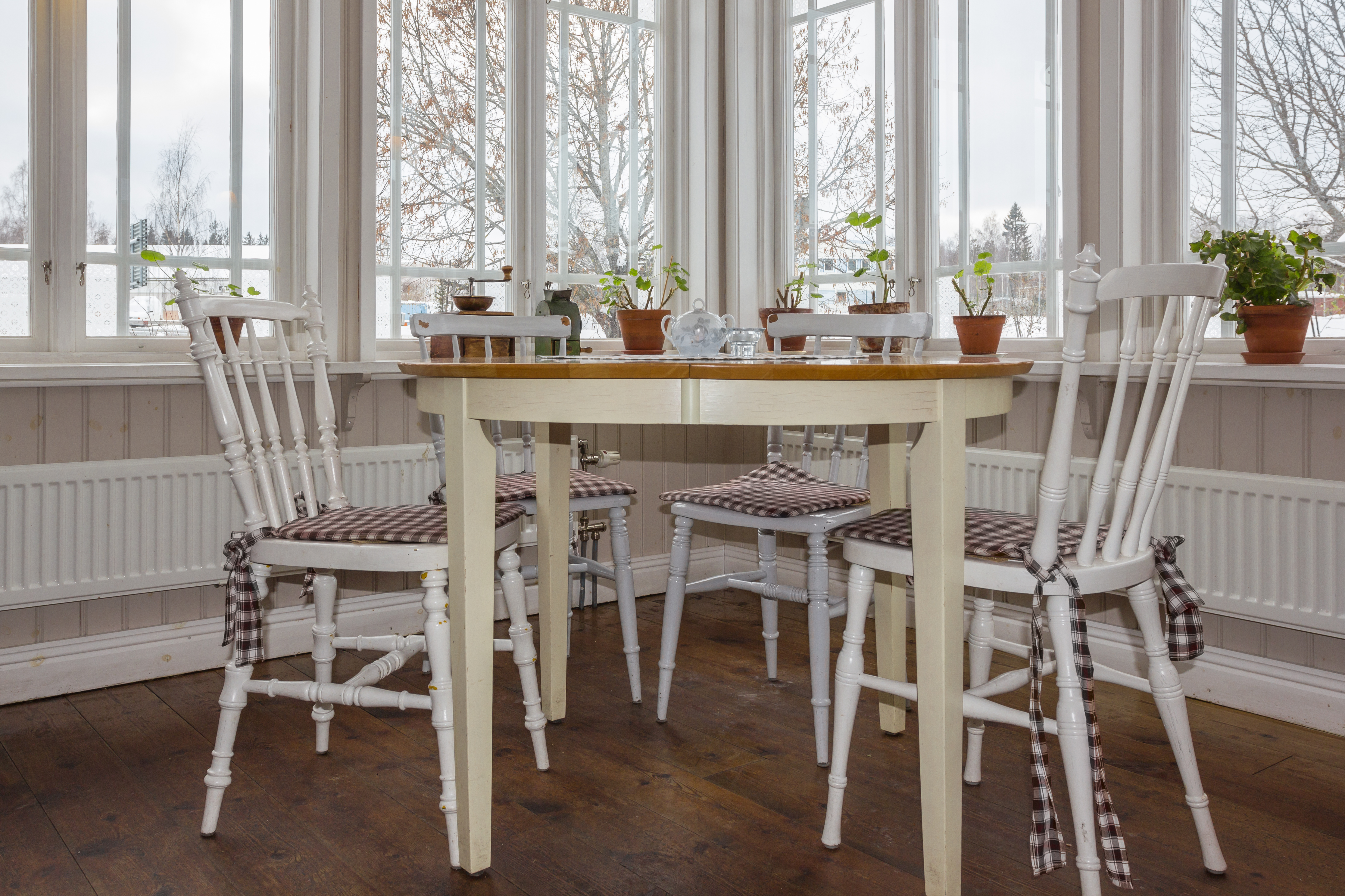 A bright cafe corner with white wooden chairs, a round table and potted plants on the windowsills