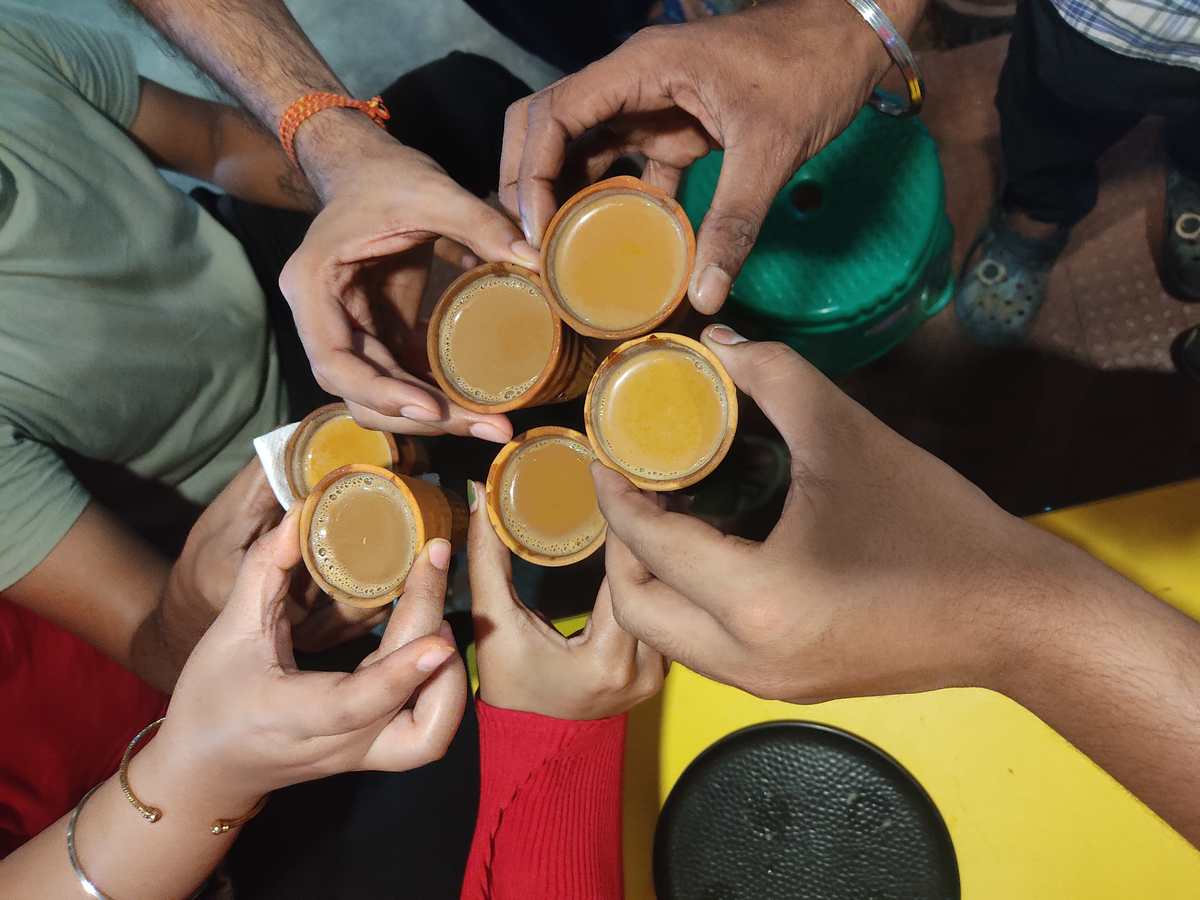 Several hands raising small clay cups of milky chai together over a table