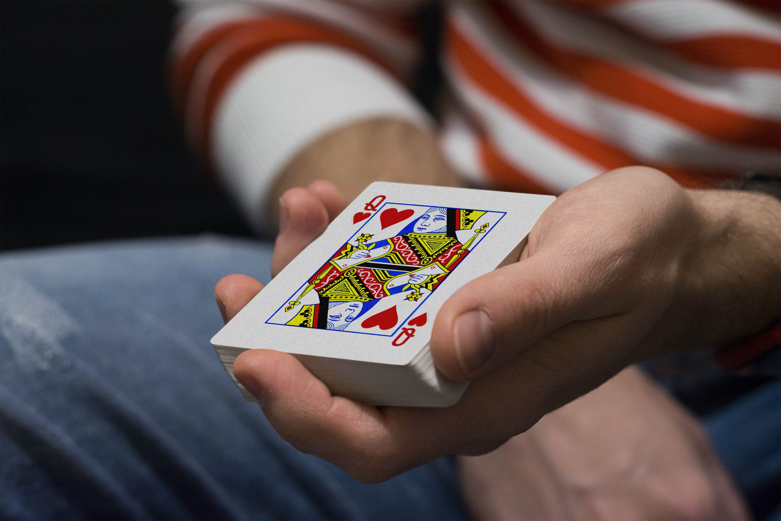 A hand holding a deck of playing cards with the queen of hearts face up on top