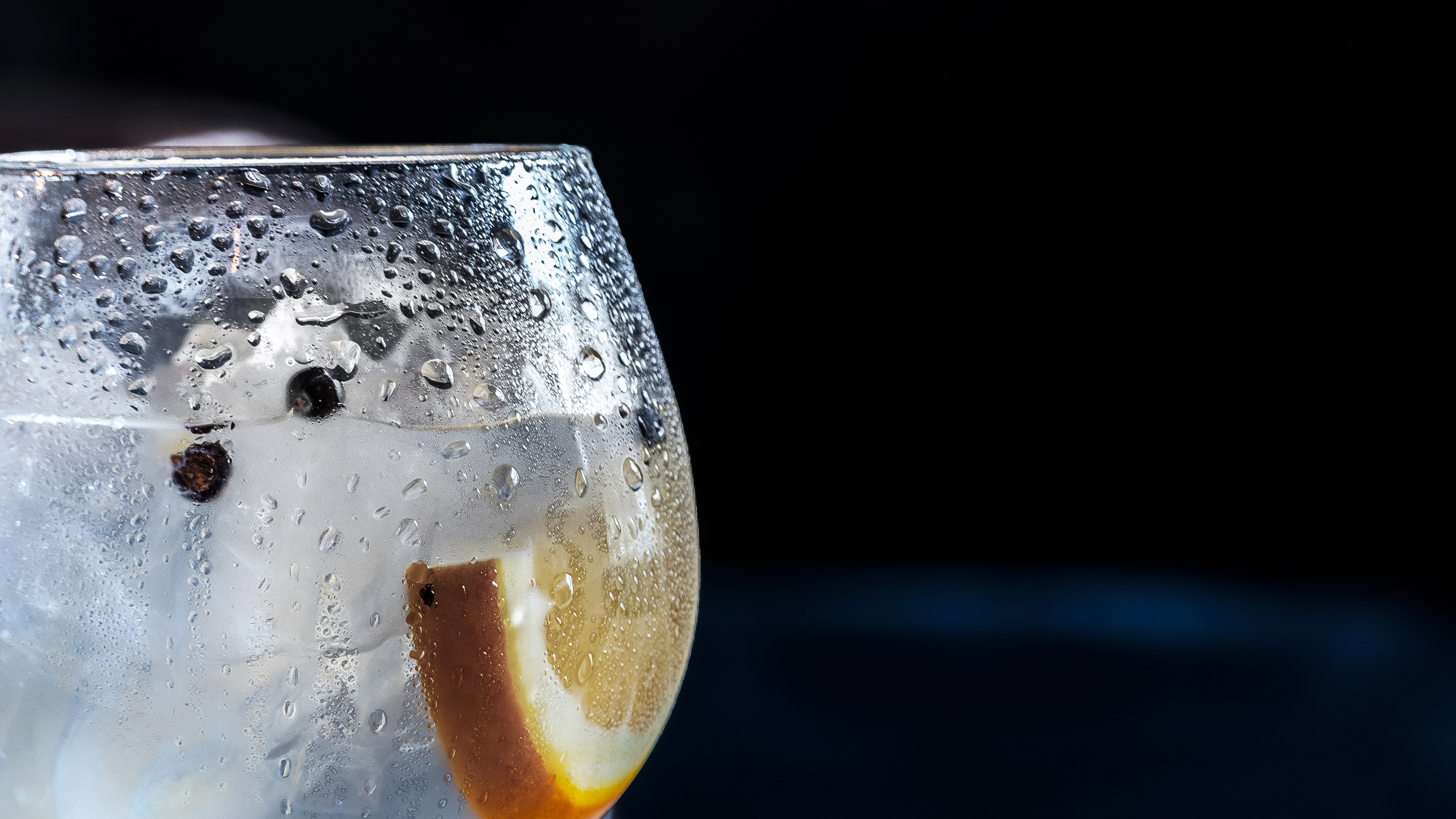 A chilled glass of sparkling drink with ice, an orange slice and a few peppercorns